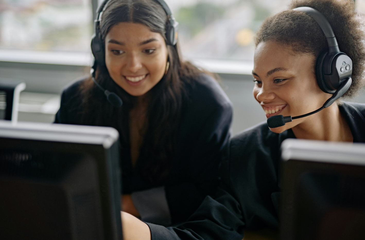 Two female employees working happily together behind monitors.