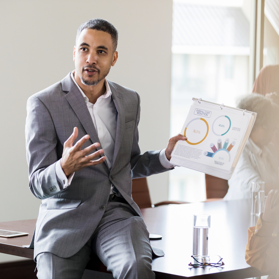 A businessman sitting at the edge of a table, presenting data.