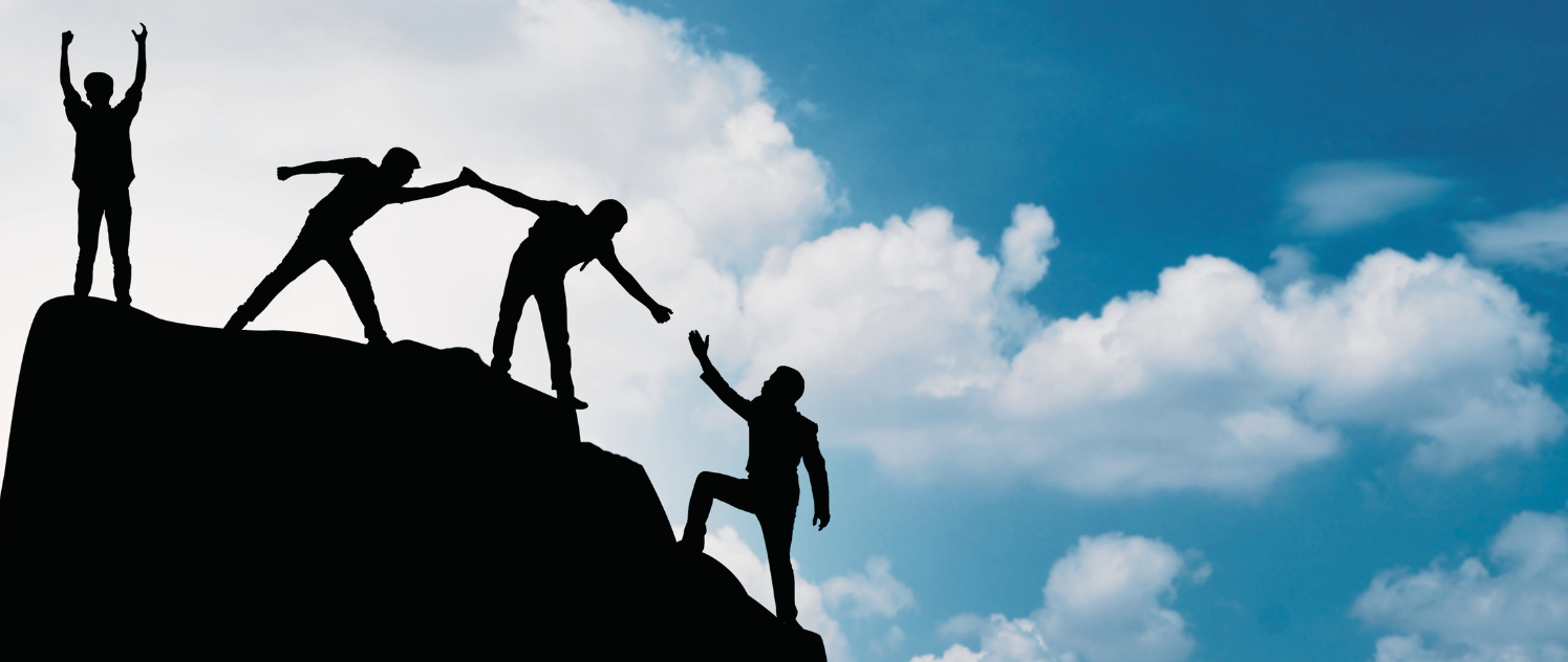 A group of hikers reaching the summit, silhouetted against a cloudy blue sky.