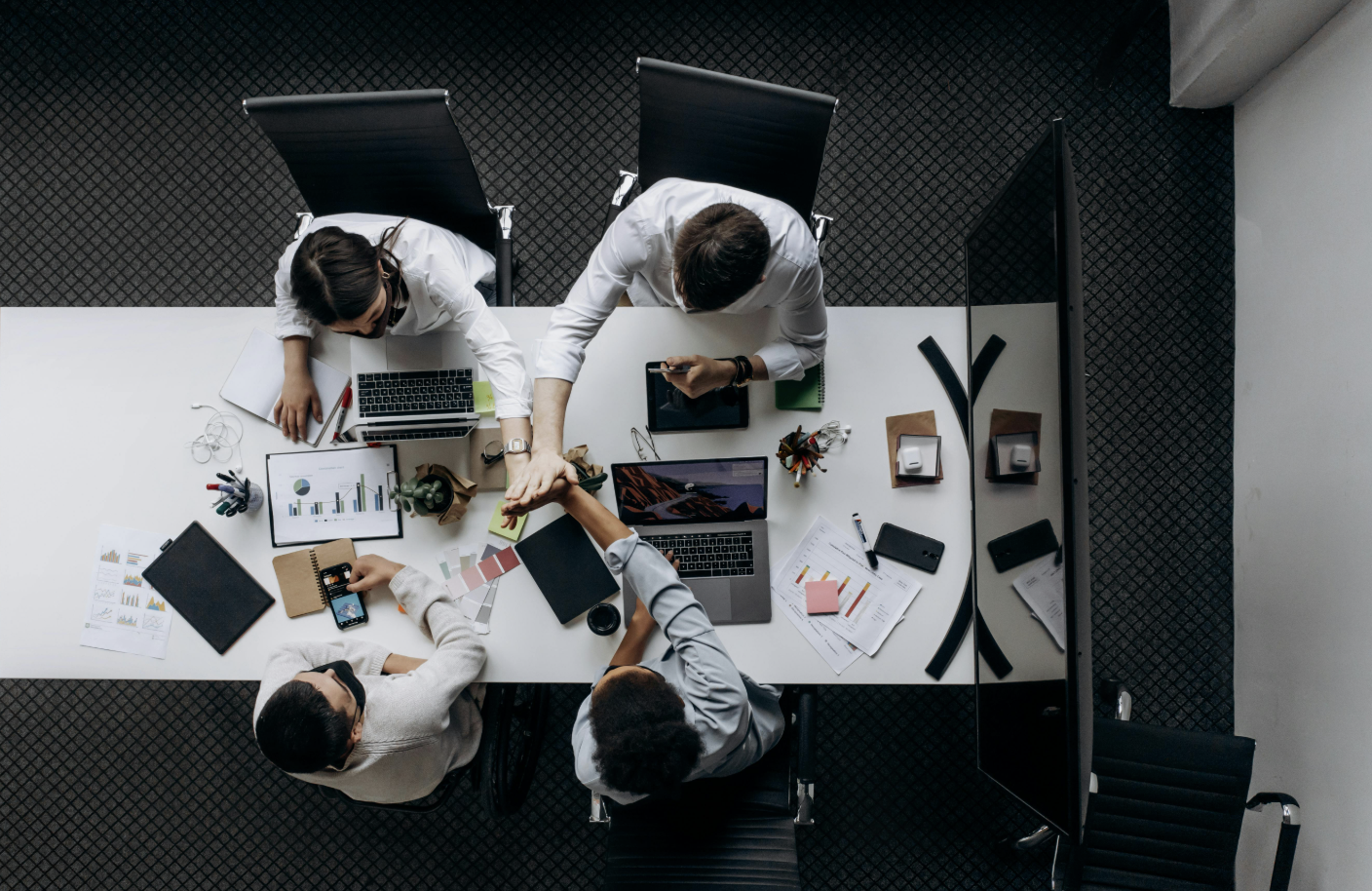 An overhead view of a team working on a project together, joining hands in a high-five.